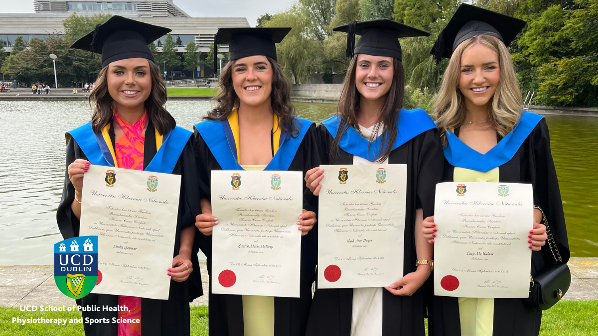 Four female graduates with scrolls in front of UCD lake